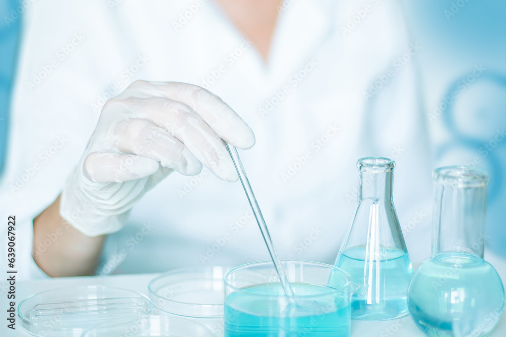 Scientific scene: Lab assistant performs tasks. Gloves and white robe worn. Glass equipment used. Clear blue liquid in play. Scientific scene: Lab assistant performs tasks. Gloves and white robe worn. Glass equipment used. Clear blue liquid in play.