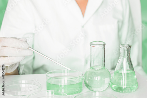 In the lab: Assistant carries out manipulations within the laboratory. Donning lab coat. Notable green hues. Using glass apparatus. Engaged in plant research in the green laboratory.