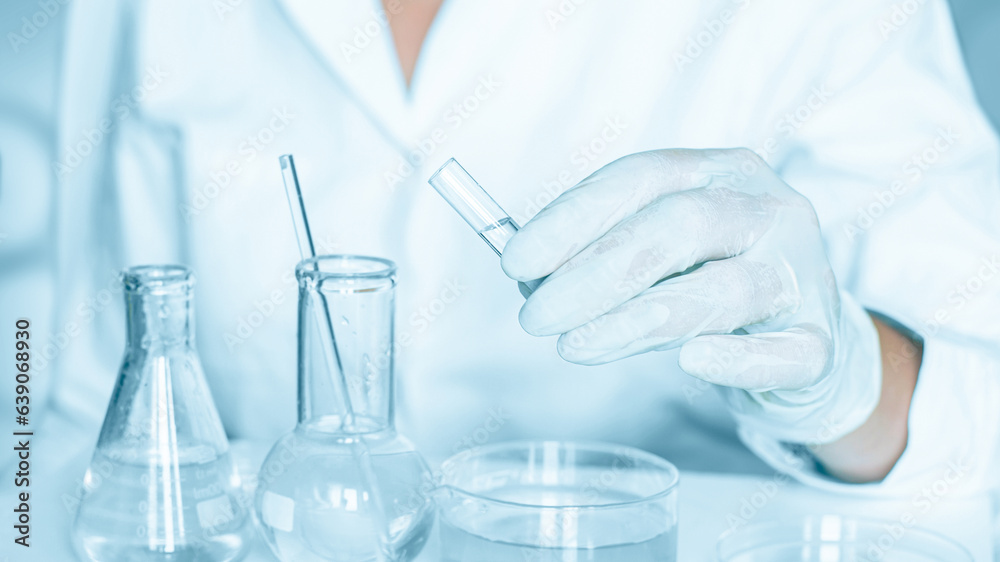 Lab backdrop: Lab assistant carries out manipulations in the laboratory atmosphere. Adorned in a lab coat. Using glass instruments. Located in a blue laboratory. Working with transparent liquid. Lab backdrop: Lab assistant carries out manipulations in the laboratory atmosphere. Adorned in a lab coat. Using glass instruments. Located in a blue laboratory. Working with transparent liquid.