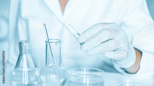 Lab backdrop: Lab assistant carries out manipulations in the laboratory atmosphere. Adorned in a lab coat. Using glass instruments. Located in a blue laboratory. Working with transparent liquid.