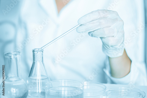 Lab backdrop: Lab assistant carries out manipulations in the laboratory atmosphere. Adorned in a lab coat. Employing glass apparatus. Blue laboratory setting. Working with transparent liquid.