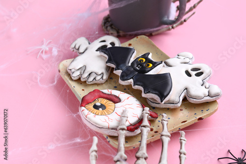 Plate with different tasty cookies and skeleton hand for Halloween celebration on pink background, closeup