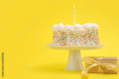 Stand with yummy Birthday cake and gift box on yellow background