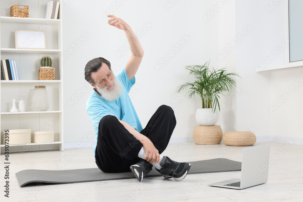 Senior man in sportswear stretching while watching online tutorial at home