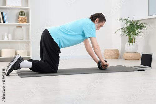 Senior man in sportswear doing exercises near laptop on fitness mat at home
