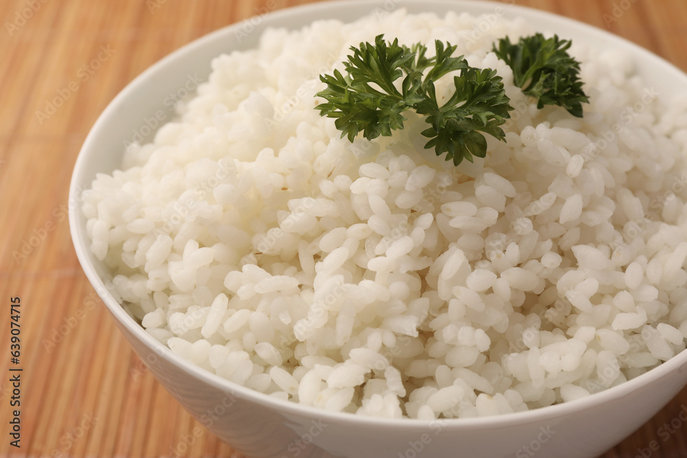 Bowl with delicious rice and parsley on bamboo mat, closeup Bowl with delicious rice and parsley on bamboo mat, closeup