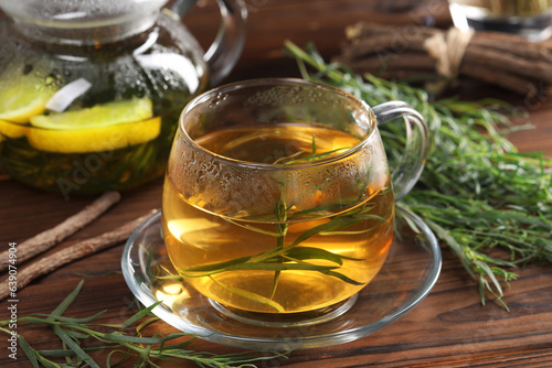 Homemade herbal tea and fresh tarragon leaves on wooden table, closeup