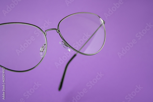 Stylish pair of glasses with metal frame on purple background, closeup