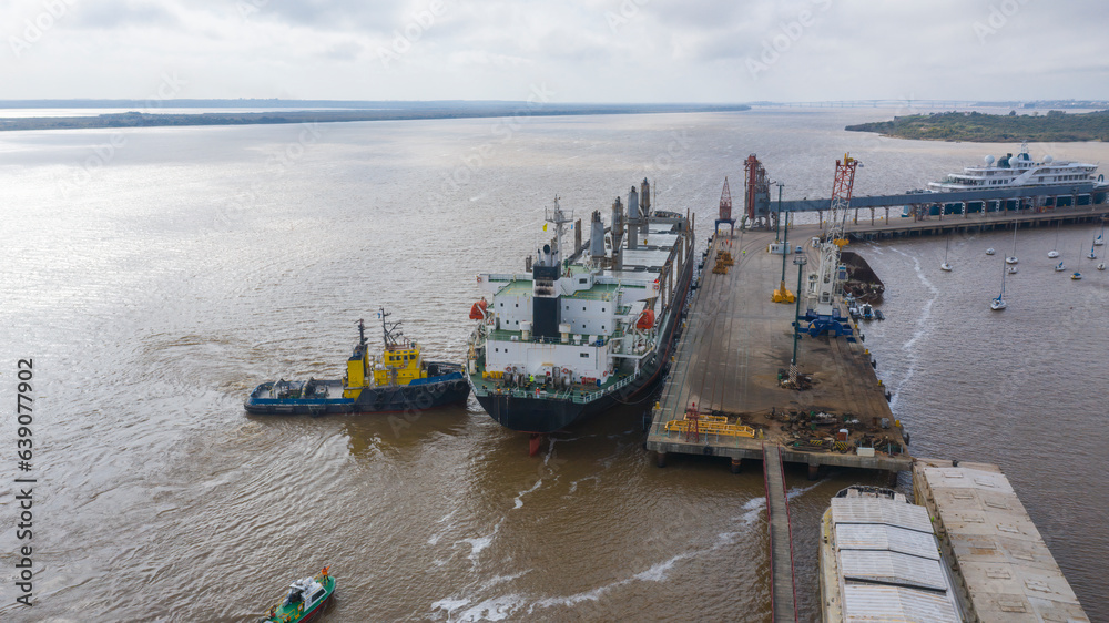 Self unloading bulk carrier arriving in South American port. Assisted by tug boat. Aerial stern view.