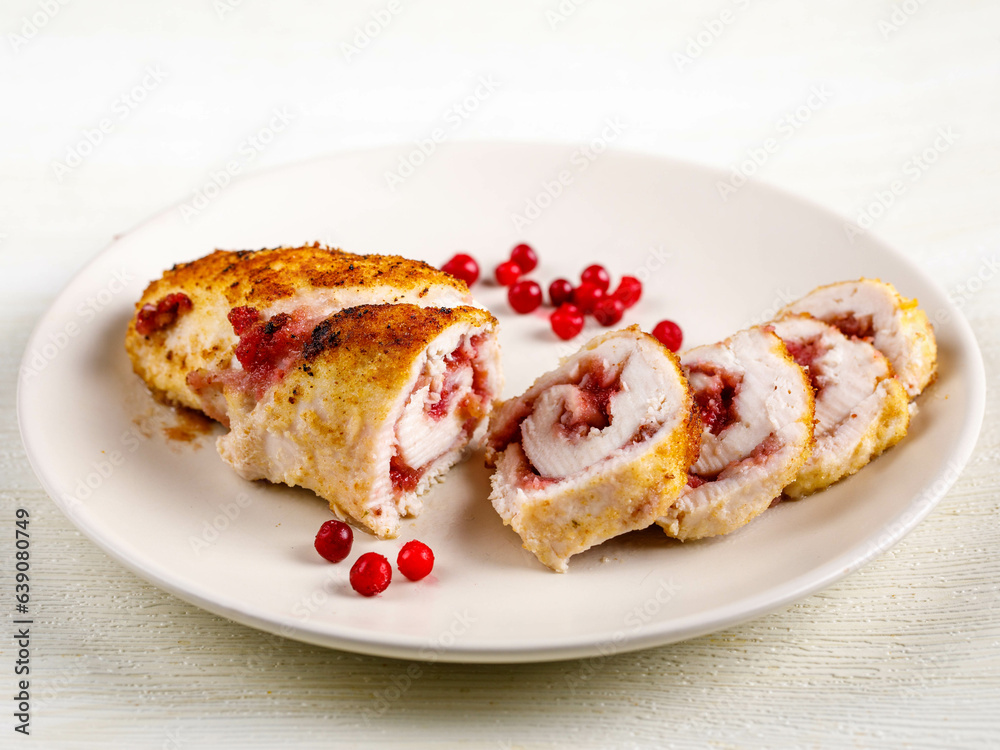 slices of delicious barbecue chicken or turkey roulade stuffed with cranberry on white dish on white wooden table, top view from above, close-up