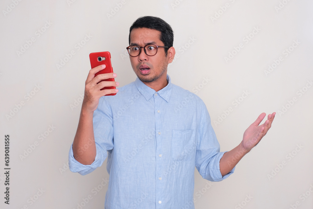 Adult Asian man showing disbelief expression when looking to his mobile phone Adult Asian man showing disbelief expression when looking to his mobile phone