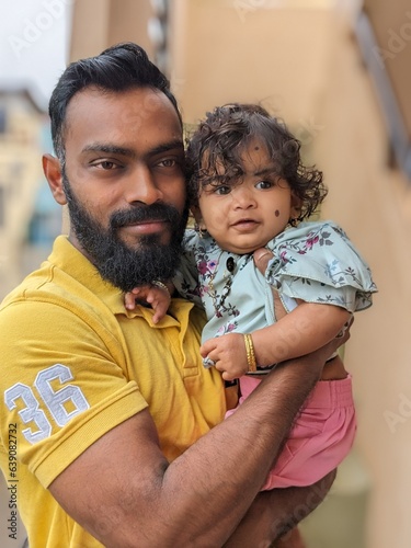 A happy, smiling uncle spends time with his niece, playing and holding the baby on his shoulder, gently supporting her. The baby smiles and holds a finger