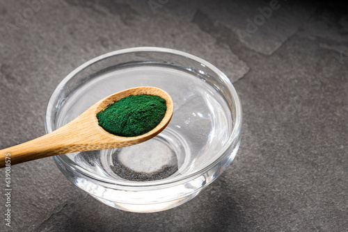 Spoon with organic spirulina powder and glass of filtered water