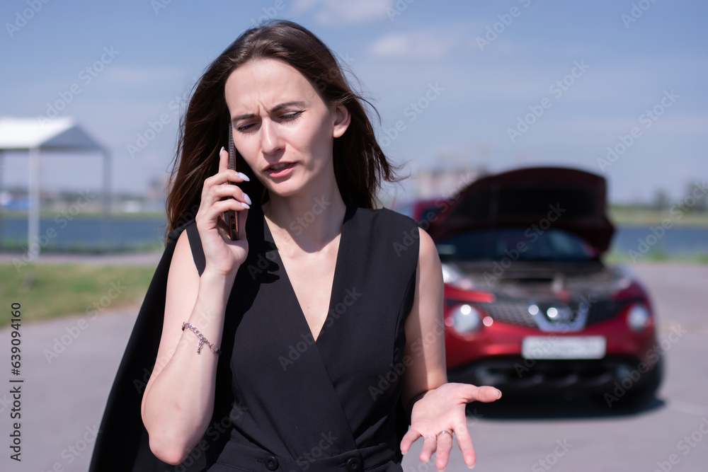Beautiful girl in a black trouser suit swears on the phone against the background of a broken car Beautiful girl in a black trouser suit swears on the phone against the background of a broken car