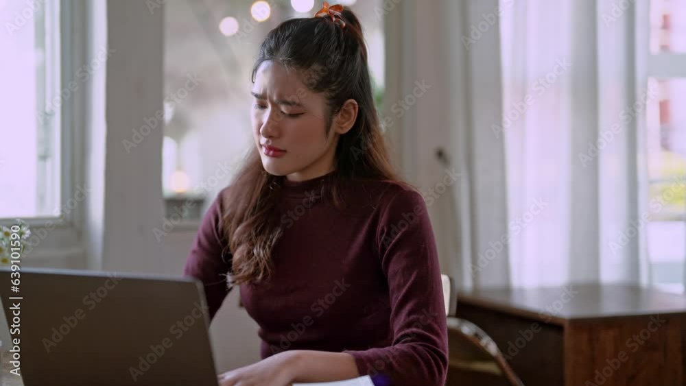tired Asian young woman seriously working on computer laptop and bored from sitting at a desk has office syndrome from work at the studio. tired Asian young woman seriously working on computer laptop and bored from sitting at a desk has office syndrome from work at the studio.