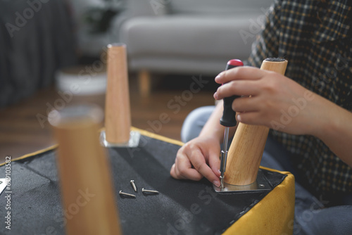 Women use screwdriver equipment to tighten screw while assembling leg of chair to making furniture