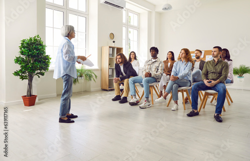 Confident mature woman speaking with a business report on a work meeting or at conference in the office in front of a small group of diverse company employees sitting on chairs in meeting room.