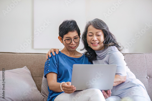 two 60s woman enjoy with social media on her laptop on a sofa