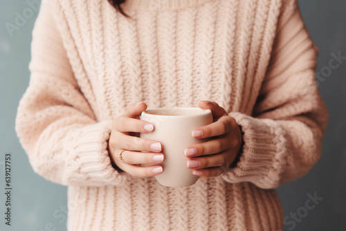 close up of woman in a cosy warm sweater holding a cup of coffee