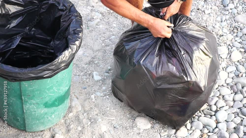 Garbage man on duty, collect garbage on beach. A janitor on the public beach takes a few big black bags of trash. Cleaner. Job. Working. Urban. Outdoor. Slow-motion, closeup, top aerial view