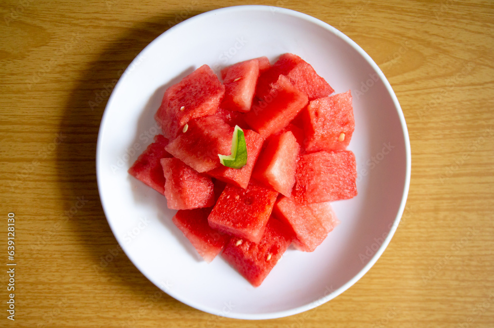 Freshly sliced watermelon on a white plate with a wood pattern background Freshly sliced watermelon on a white plate with a wood pattern background