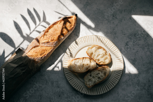 French fresh bread baguette with slices on a ceramic plate on gray background.