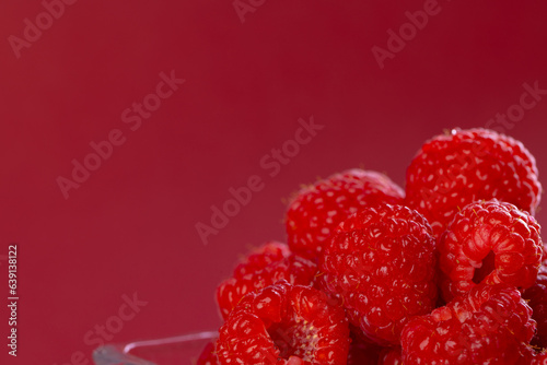 Micro close up of raspberries in glass bowl with copy space on red background