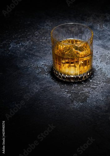 Whiskey glass with ice cubes in middle of black background.
