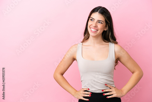 Young Italian woman isolated on pink background posing with arms at hip and smiling