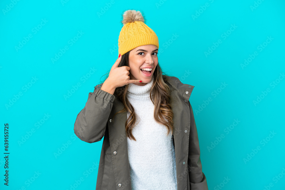 Young Italian woman wearing winter jacket and hat isolated on blue background making phone gesture. Call me back sign Young Italian woman wearing winter jacket and hat isolated on blue background making phone gesture. Call me back sign