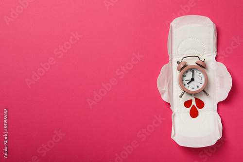 Menstrual pad with clock and red drops on pink background photo