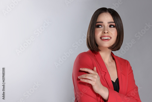 Portrait of stylish young woman with brown hair smiling on grey background, space for text