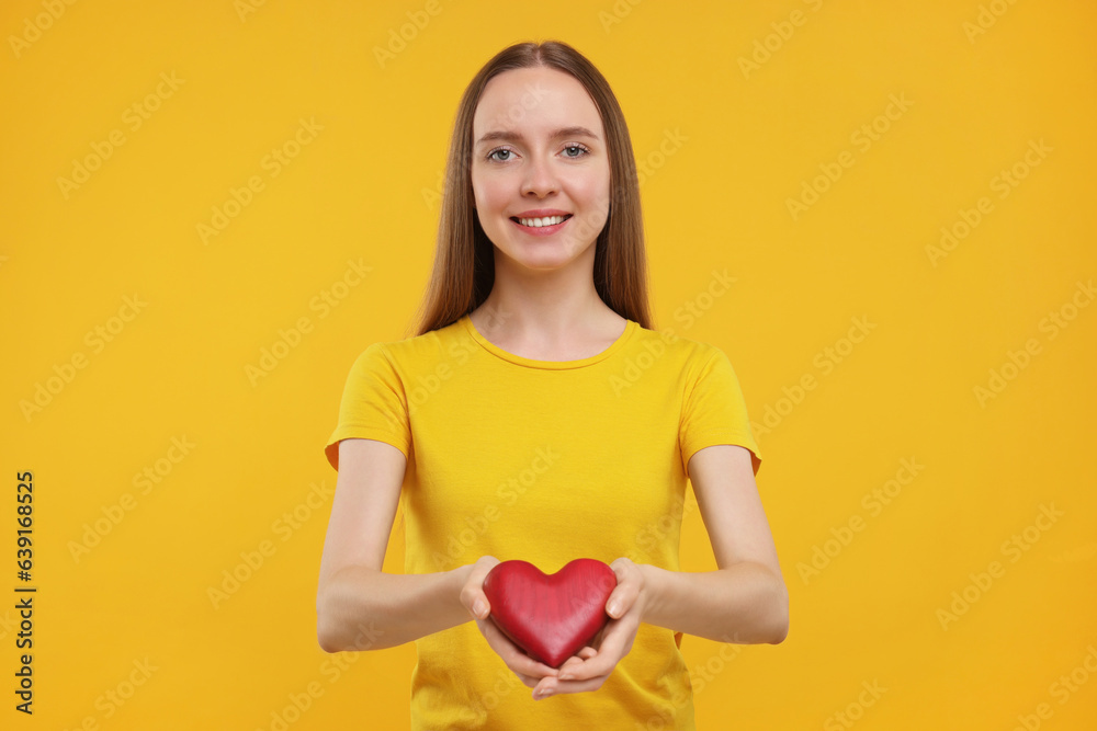 Happy young woman holding red heart on yellow background Happy young woman holding red heart on yellow background