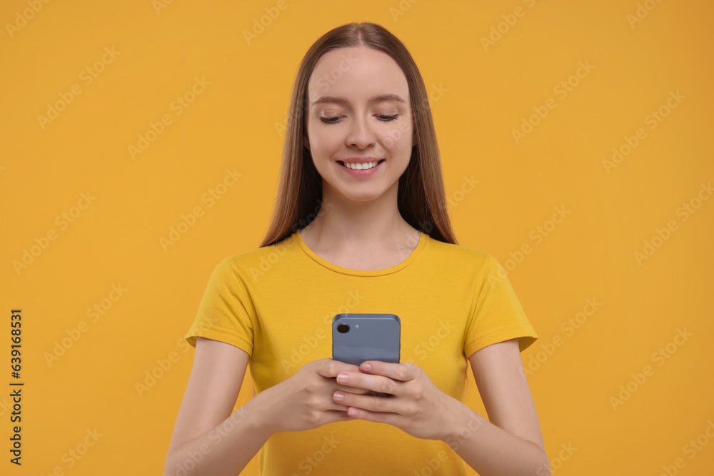 Happy young woman using smartphone on yellow background