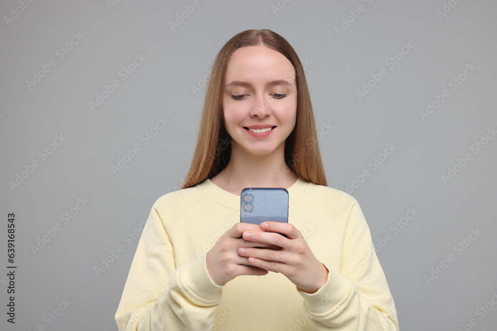 Happy young woman using smartphone on light grey background Happy young woman using smartphone on light grey background