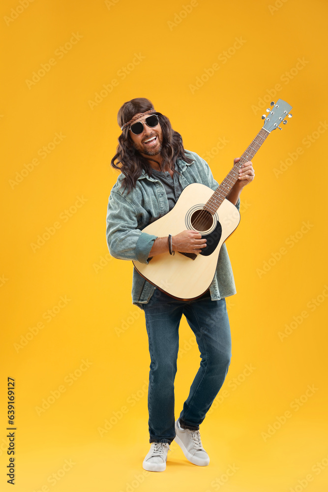 Stylish hippie man playing guitar on orange background Stylish hippie man playing guitar on orange background