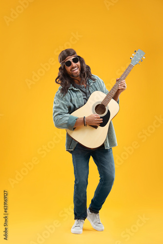 Stylish hippie man playing guitar on orange background