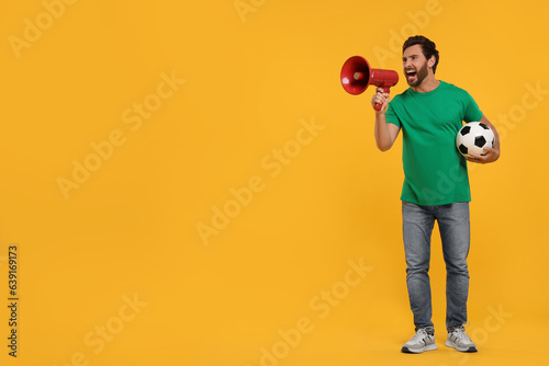 Emotional sports fan with soccer ball and megaphone on orange background, space for text