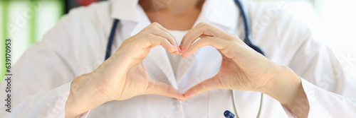 Smiling female doctor showing heart gesture close up.