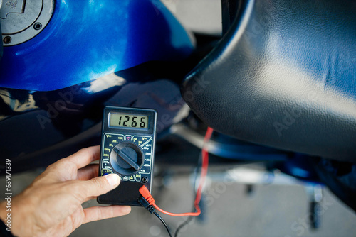 Obraz na płótnie motorcycle battery voltage diagnostics with a multimeter. w salonie