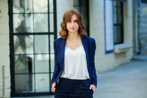 Portrait of a beautiful young woman with long brown hair, dressed in a blue jacket, standing against the background of an office building. strong and confident business woman
