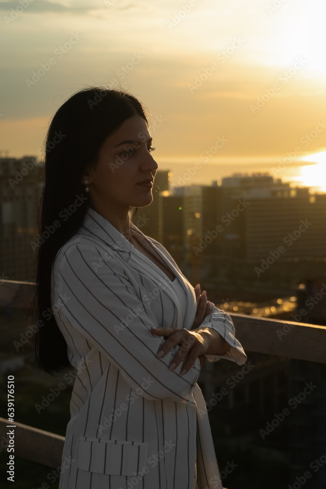 Beautiful young business woman on a construction site against the background of the sea and sunset. Concept of the construction industry, professions, construction business. Vertical photo