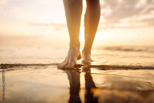 Close-up young woman's legs walking on a wave of sea water and sand on the beach. The concept of vacation, travel, freedom.