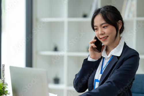 Asian businesswoman using mobile phone to communicate, chat, negotiate, search internet, news, email while working online on laptop computer at office.