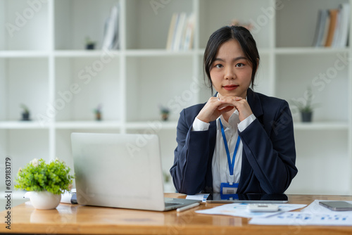 Asian businesswoman standing working with laptop computer, mobile phone, tablet to contact, chat, search internet, news, email, chat while working on finance, marketing, accounting data in office.