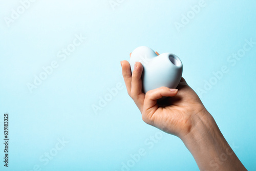 Female hand is holding blue vacuum clitoral stimulator in the shape of a heart on a blue background. Place for text. Sex shop concept. Copy space