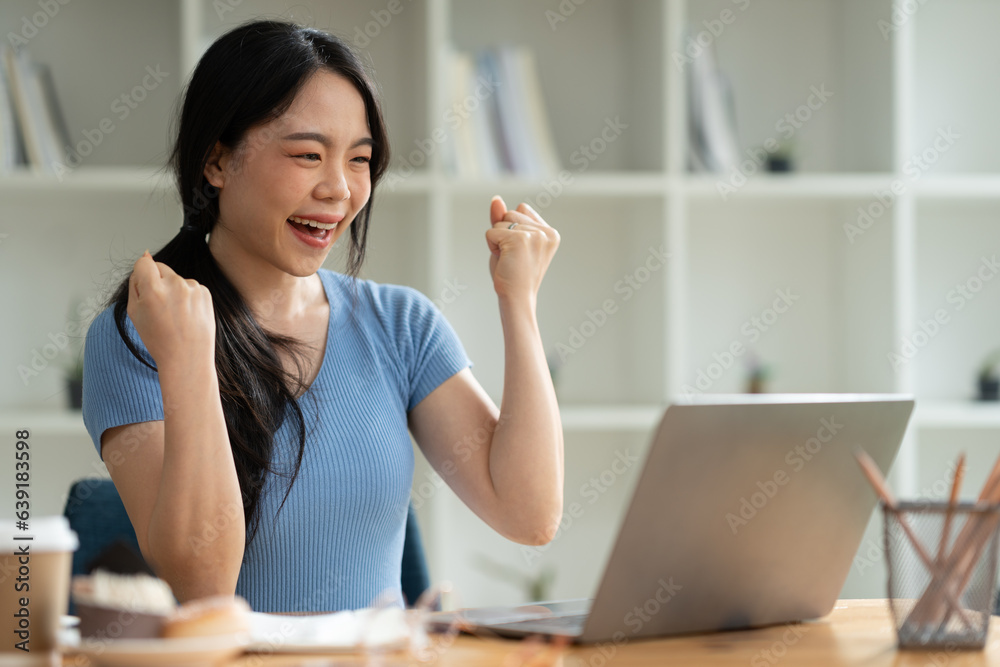 Asian woman sitting at work happily, smiling, delighted with business success feedback data from smartphone and data on laptop. while sitting on a desk in his office at home Asian woman sitting at work happily, smiling, delighted with business success feedback data from smartphone and data on laptop. while sitting on a desk in his office at home