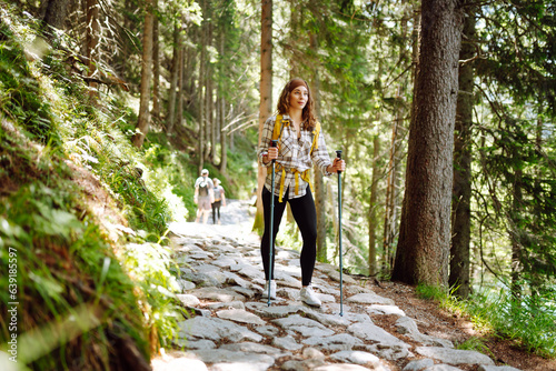 Hiking. Female traveler with a yellow backpack and hiking poles travels along a trail in the mountains. Active lifestyle. © maxbelchenko