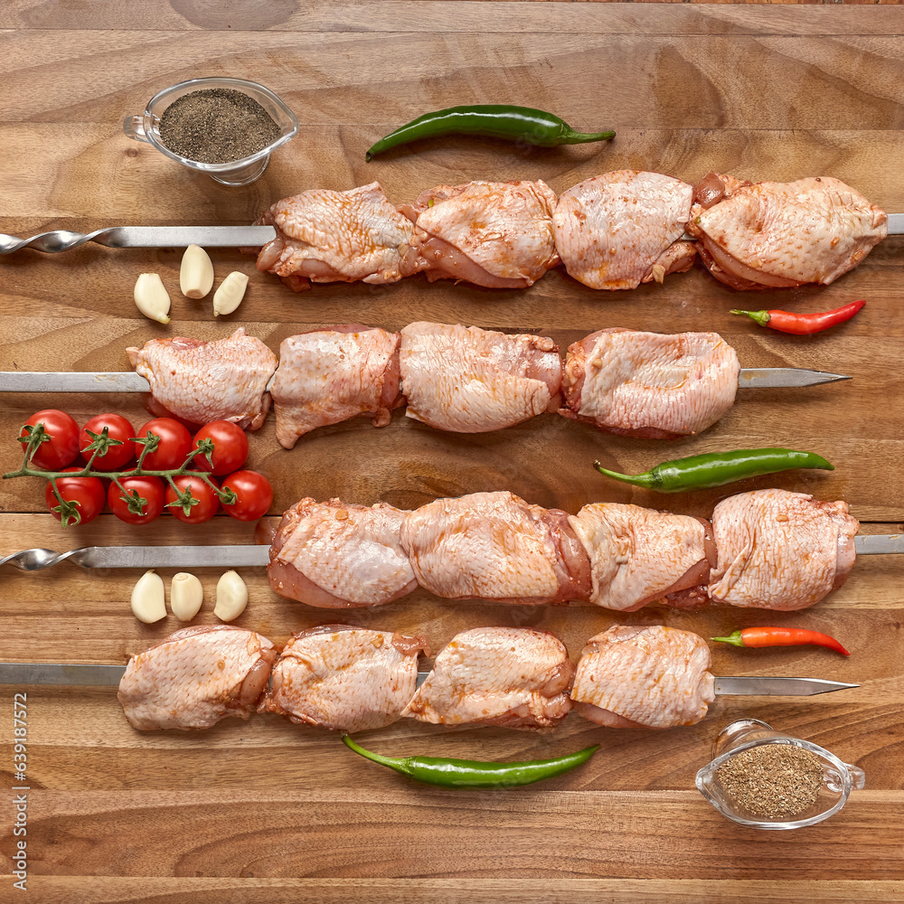 Metal skewers with raw uncooked chicken meat for frying on the wooden board with peppers near it, top view flatlay Metal skewers with raw uncooked chicken meat for frying on the wooden board with peppers near it, top view flatlay