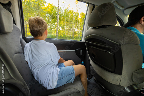 The boy looks out the open car window. The family travels around the country in Manish on vacation. The family spends time traveling in their minivan during the summer. Family travel concept by car. photo
